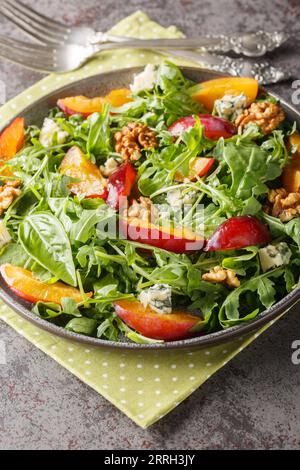 Fresh salad of plums, arugula, gorgonzola cheese and walnuts close-up in a plate on the table. Vertical Stock Photo