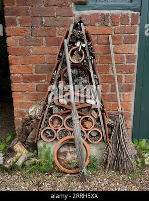 A Rustic Bug Hotel made out of old pots and pipe with a wooden broom in front of a brick wall. Stock Photo