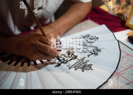 220630 -- CHANGSHA, June 30, 2022 -- A painter draws patterns on a fan at the Yueyang tower scenic spot in Yueyang City, central China s Hunan Province, June 23, 2022. Yuezhou fan dates back to the late Ming Dynasty 1368-1644 and early Qing Dynasty 1644-1911. The fan, having a history of about 400 years, is one of the most famous fans in China for its delicacy. Using fine bamboo as its framework, ox horn as the nail, and Xuan paper as the cover, the fan goes through 72 complicated procedures before done, while the making of framework requires most exquisite and skillful work. The crafts of mak Stock Photo