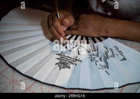 220630 -- CHANGSHA, June 30, 2022 -- A painter draws patterns on a fan at the Yueyang tower scenic spot in Yueyang City, central China s Hunan Province, June 23, 2022. Yuezhou fan dates back to the late Ming Dynasty 1368-1644 and early Qing Dynasty 1644-1911. The fan, having a history of about 400 years, is one of the most famous fans in China for its delicacy. Using fine bamboo as its framework, ox horn as the nail, and Xuan paper as the cover, the fan goes through 72 complicated procedures before done, while the making of framework requires most exquisite and skillful work. The crafts of mak Stock Photo