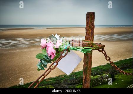 Plastic memorial flowers attached to chain on seawall fence Stock Photo