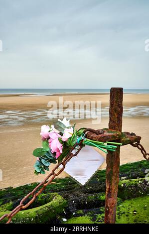 Plastic memorial flowers attached to chain on seawall fence Stock Photo