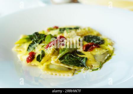 Italian ravioli pasta with basil, spinach, sun-dried tomatoes, pine nuts and cheese in a white plate. Traditional Italian cuisine in the restaurant Stock Photo