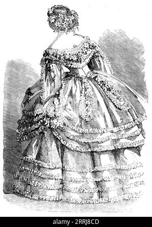 Fashions for November - Robe of White Crape over a slip of White Satin, 1858. 'The robe has a double skirt trimmed with ruches of blonde, four rows on the lower and three on the upper skirt. The corsage is plain, and pointed in front and at the back. Over it is a fichu Antoinette, covered with ruches of blonde, through the midst of which there runs a wreath formed of honeysuckle and pink azalea. The upper skirt is gathered up at each side by a chatelaine of the same flowers. Odalisque sleeves, gathered up in front of the arm by bouquets of honeysuckle and azalea. A narrow cordon of the same fl Stock Photo