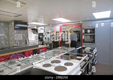 A salesman demonstrates an electric oven to a female customer in a kitchen appliance store in south London, UK. Stock Photo
