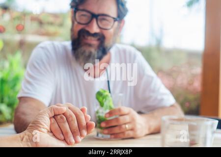 Happy man holding woman hand in pov. Focus on hands. Love and dating. Relationship adult people in love. Family on vacation sitting at the bar. Defocused background of male smiling having fun and wife Stock Photo