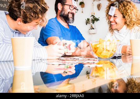 Happy real people family play together with cards at home on the table laughing and having fun. Man and woman father mother with son enjoy time in playful indoor leisure activity on sunday holiday Stock Photo