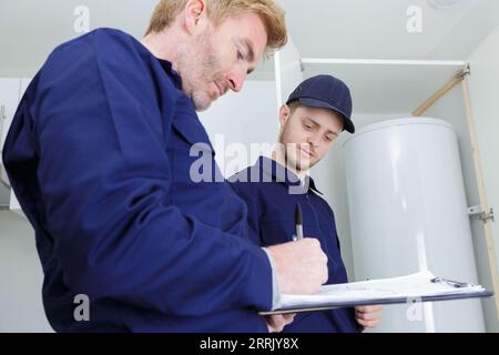 plumber writing on clipboard by electric boiler Stock Photo