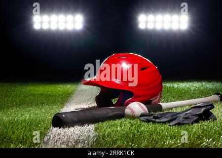 Red batting helmet bat baseball and gloves on grass field with stripe under stadium lights at night Stock Photo