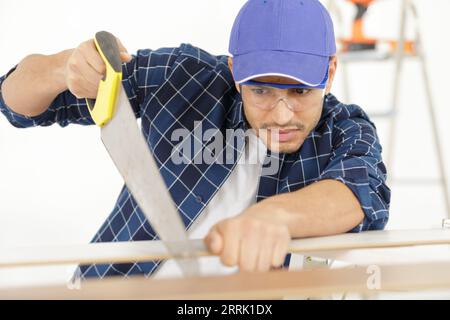 man carpenter cuts a wooden beam using handsaw Stock Photo