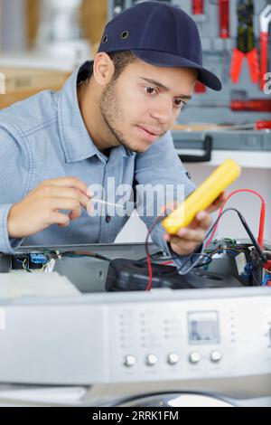young serviceman testing washing machine with multimeter Stock Photo