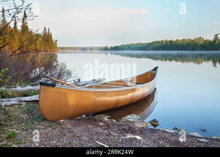 Yellow canoe on the shore of a calm northern Minnesota lake in early morning light Stock Photo