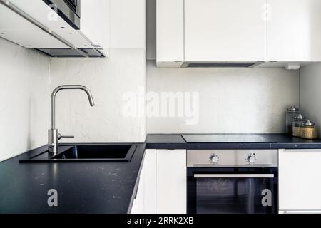 Kitchen interior. Modern white and black design. Scandinavian minimalist lifestyle. Induction cooker and stove, electric oven in new apartment. Stock Photo
