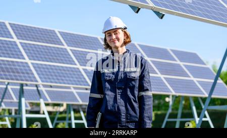 Female engineer holding laptop checking solar panels at solar farm Stock Photo
