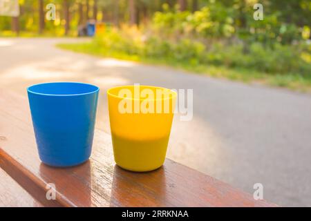 Blue and yellow cups with coffee in morning sunshine. Patriotic ukrainian colours. Two plastic mugs with cappuccino. Portable camping cups. Stock Photo