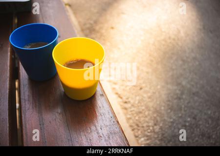 Blue and yellow cups with coffee in morning sunshine. Patriotic ukrainian colours. Two plastic mugs with cappuccino. Portable camping cups. Stock Photo