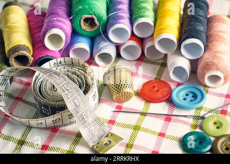 Sewing kit consisting needle, thimble, threads and measuring meter on a fabric background Stock Photo
