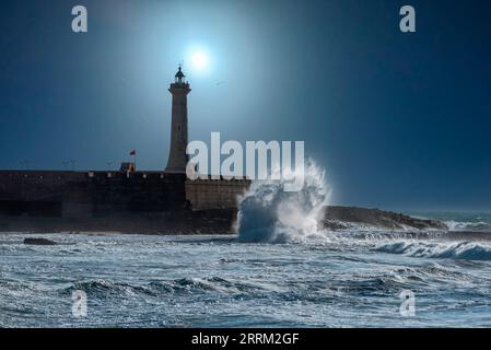 The moon shines over a picturesque lighthouse at night, waves break at the coast Stock Photo