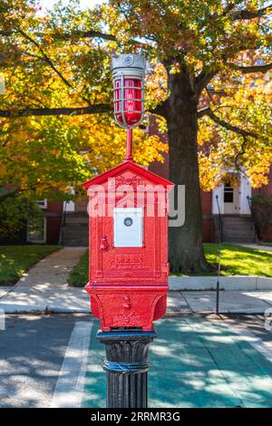 Traditional Boston fire alarm station box - manufactured by Game Well - on a pedestal in front of beautiful fall trees on a sunny fall day Stock Photo