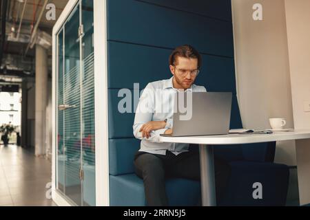 Focused freelancer drinking coffee during working on laptop in modern coworking  Stock Photo