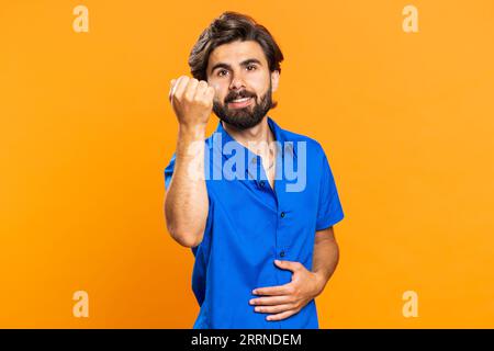 Knock-knock who is there. Confused young man knocking door gesture asking who is at home, feeling embarrassed, no idea, being clueless and uncertain. Arabian guy isolated on orange studio background Stock Photo