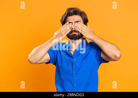 Dont want to look at this, awful. Afraid middle eastern man closing eyes with hand showing stop gesture, confused shy scared to watch. Young guy isolated on orange studio background. People lifestyles Stock Photo