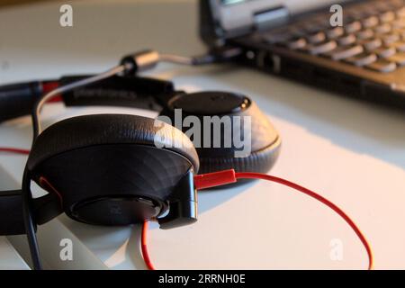 A photo of a pair of black and red headphones on a desk beside a computer. Stock Photo