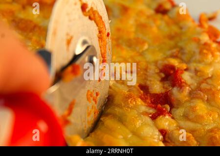 A photo of some cutting up a margerita pizza with a pizza cutter. Stock Photo