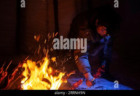 230113 -- GENHE, Jan. 13, 2023 -- Dalinma, Juele s cousin, cooks roasted meat for dinner in a traditional Ewenki tent at a temporary herding station at the Jinhe forest range near Genhe City, north China s Inner Mongolia Autonomous Region, Jan. 11, 2023. Every two or three days, Juele Bulituotian will head for the Jinhe forest range about 80 kilometers from Genhe City. That s where the 39-year-old Aoluguya Ewenki herder, wearing a traditional fur coat, will find his foraging reindeer. Instead of keeping reindeer in a barn, Ewenki herders let the animals live in the forest and check on them eve Stock Photo