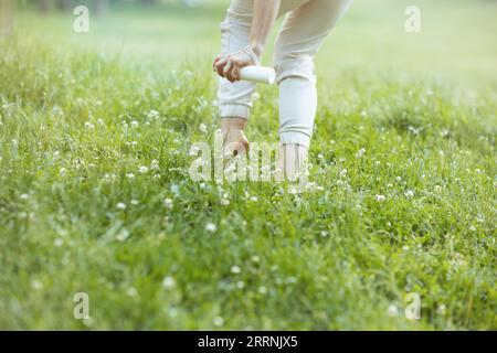 Summer time. Closeup on elegant female in white shirt using mites spray in the meadow in the city park. Stock Photo