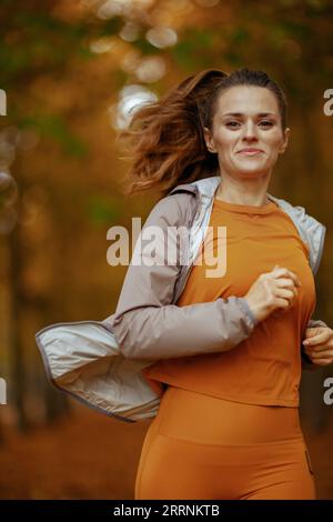 Hello autumn. fit middle aged woman in fitness clothes in the park running. Stock Photo