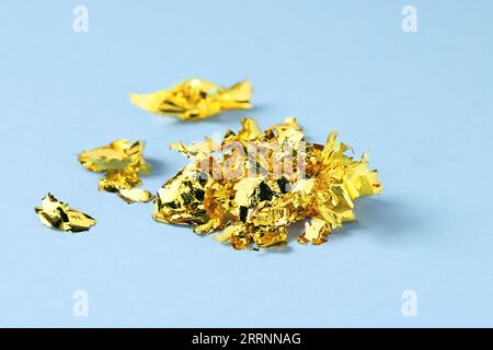 Many pieces of edible gold leaf on light blue background, closeup Stock Photo