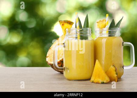 Tasty pineapple smoothie in mason jars on wooden table against blurred background, space for text Stock Photo