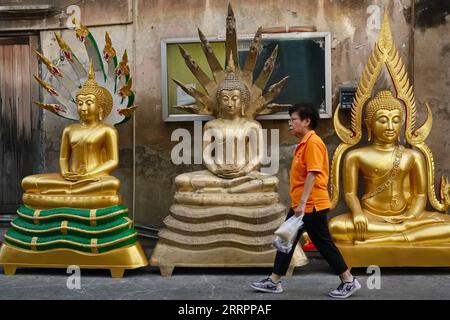 A Thai woman walks past three golden Buddha statues placed outside a factory for Buddhist paraphernalia in Bamrung Muang Road, Bangkok, Thailand Stock Photo