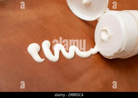 Applying white cream from an opened tube on brown leather , soft focus close up, abstract backdrop Stock Photo