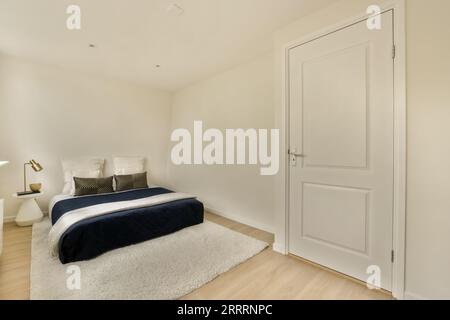 a bedroom with white walls and hardwood flooring the room has a bed, two nightstands and a window Stock Photo