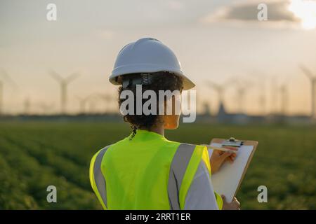 Back view of woman engineer in white helmet working with clipboard at renewable energy farm Stock Photo