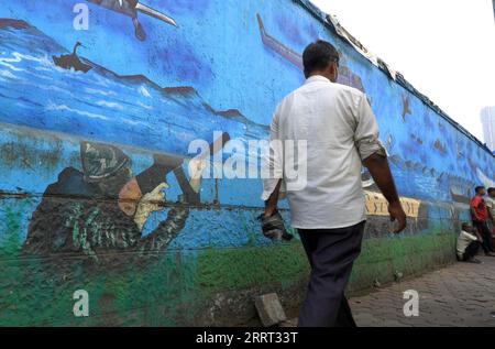 A pedestrian walks past a painted wall featuring military warfare in Mumbai India Stock Photo