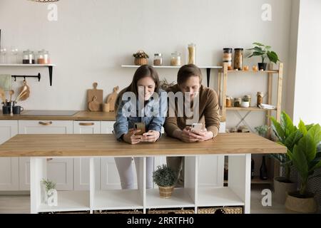 Positive digital addicted couple standing close in kitchen Stock Photo