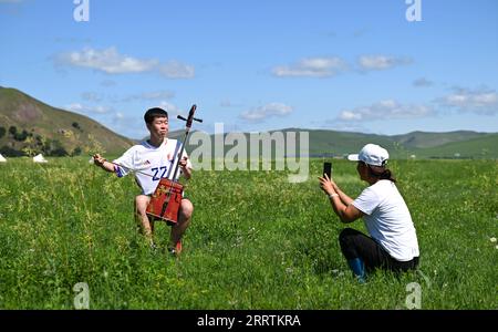 230730 -- HINGGAN LEAGUE, July 30, 2023 -- Bai Saran, wife of Uu Sodo, takes photos of her son Uu Surleg while he is playing the Morin Khuur, in Horqin Right Wing Front Banner, Hinggan League, north China s Inner Mongolia Autonomous Region, July 24, 2023. Uu Sodo, a herdsman, and his family reside in a village on the Ulan Mod grassland, located in Horqin Right Wing Front Banner, Hinggan League of north China s Inner Mongolia Autonomous Region. Earlier this year, Uu Sodo established a herdsman house hostel , offering guests the opportunity to try horse riding, archery, savor milk tea and mutton Stock Photo