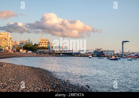 Sunset over the small picturesque town nesting a pebble beach near the local harbor Marina del Sur with lots of boats docked or moored, Las Galletas Stock Photo