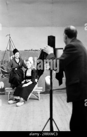 Ein Studiofotograf fotografiert zwei junge Frauen in Tracht vor einem gemalten Hintergrund, Volendam 1941. A studio photographer takes pictures of two young women in traditional costume against a painted background, Volendam 1941. Stock Photo