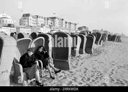 Zwei Frauen sitzen in Strandkörben am Strand von Scheveningen, Niederlande 1955. Two women sitting in the beach chairs on the beach at Scheveningen, Netherlands 1955. Stock Photo