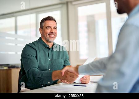 Smiling middle aged business man handshaking partner at office meeting. Stock Photo