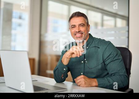 Happy mid aged professional business man sits at work desk in office, portrait. Stock Photo