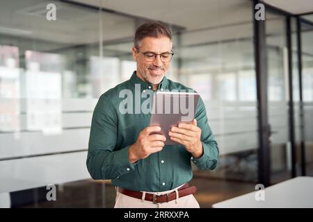 Smiling busy middle aged business man investor using tablet standing in office. Stock Photo