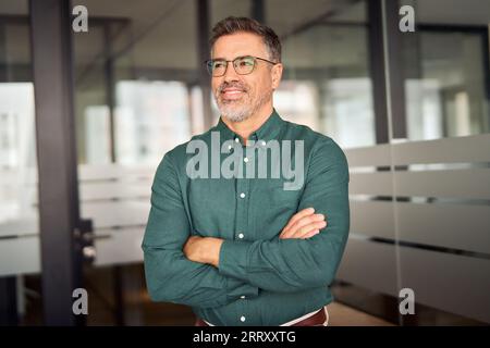 Successful middle aged business man looking aside standing in office. Stock Photo