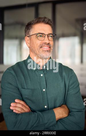 Smiling mature business man looking away standing in office. Vertical Stock Photo