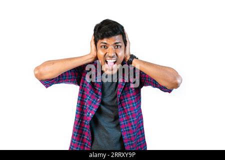A young man with short brown hair and glasses is surprised and covering his ears with his hands. He is giving a thumbs up with his right hand. The bac Stock Photo