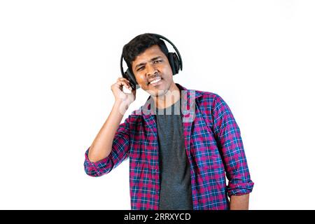 A young man with headphones on is dancing in front of a plain background. He is smiling and looking at the camera Stock Photo